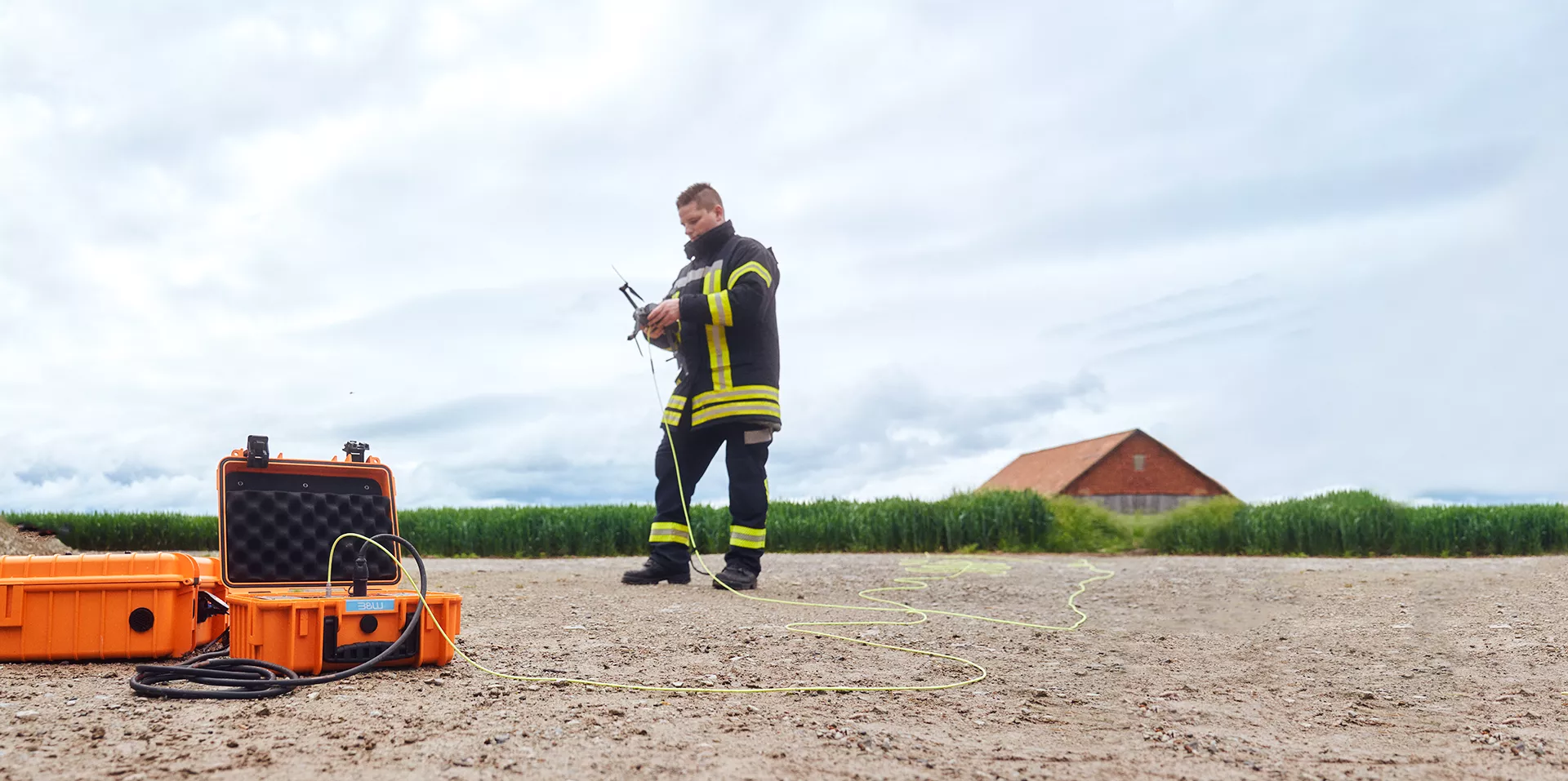 Firefighter has a drone in his hand, in front of it is an open orange case with the battery for the drone inside.